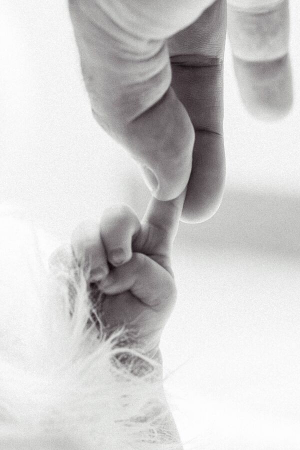 Papas Hand hält den kleinen Babyfinger beim Newbornshooting in Lauf