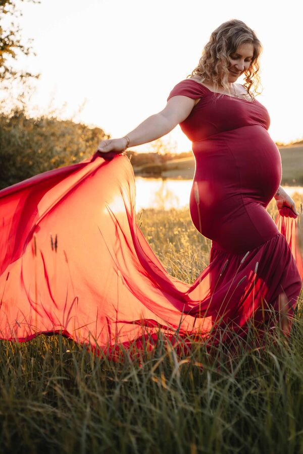 Babybauch in rotem Kleid am See